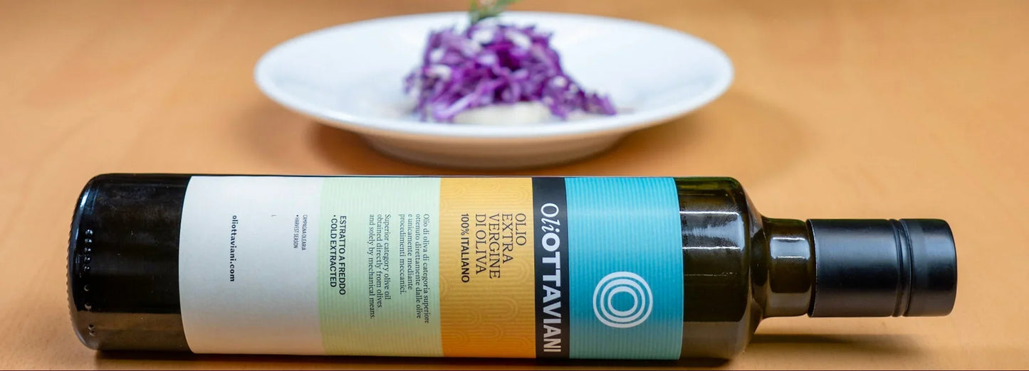 Bottiglia di olio extra vergine di oliva italiano OiO.TTAVIANI su piano legno con piatto e cavolo rosso